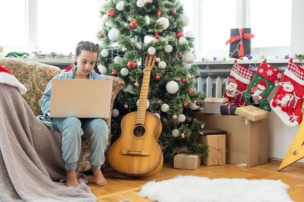 menina sentada, olhando para um laptop com um sorriso antes do Natal. - Foto, Imagem