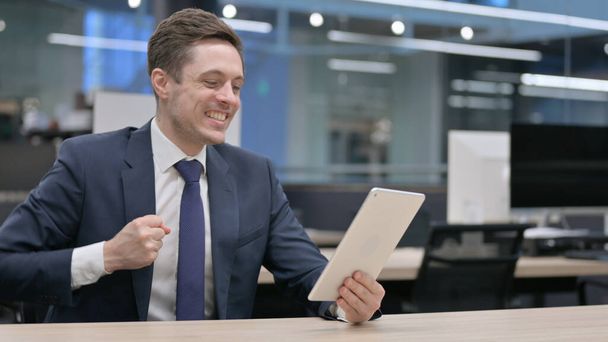 Jonge zakenman vieren succes op Tablet in Office, Zitten - Foto, afbeelding