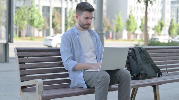 Чоловік використовує ноутбук, сидячи на лавці
 - Фото, зображення