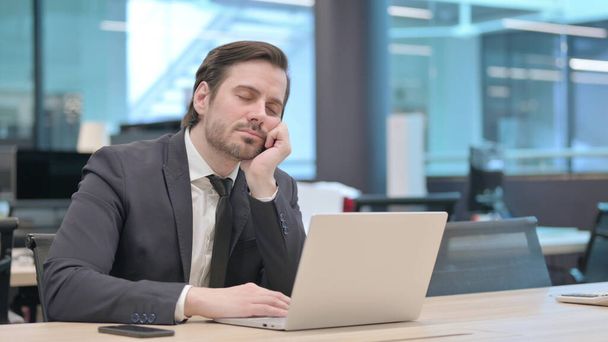 Joven hombre de negocios cansado tomando siesta mientras está sentado en la oficina con el ordenador portátil - Foto, Imagen
