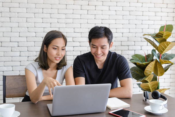 Young asian couple wear casual clothing relaxing while sitting in kitchen room and working with computer laptop at home. Love, happiness, work at home concept - Фото, зображення