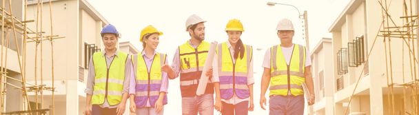 Grupo de contratistas felices, ingenieros y formatos en chalecos de seguridad con cascos están de pie en el sitio de construcción en construcción. concepto de trabajo en equipo - Foto, imagen