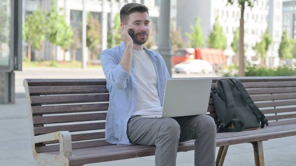 Man Talking on Phone and using Laptop while Sitting on Bench - Foto, Imagen