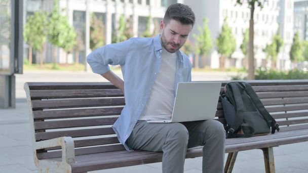 Man with Back Pain Using Laptop while Sitting on Bench - 写真・画像