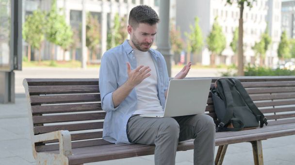 Man Reacting to Loss on Laptop while Sitting on Bench - Foto, afbeelding