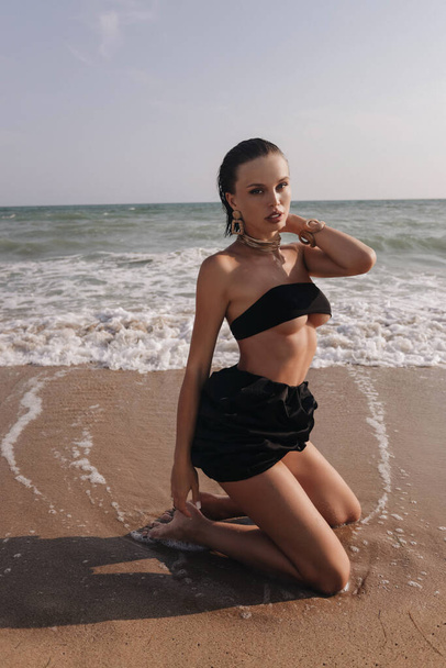 fashion outdoor photo of beautiful woman with dark hair in elegant clothes posing  on the summer beach at sunset - Valokuva, kuva
