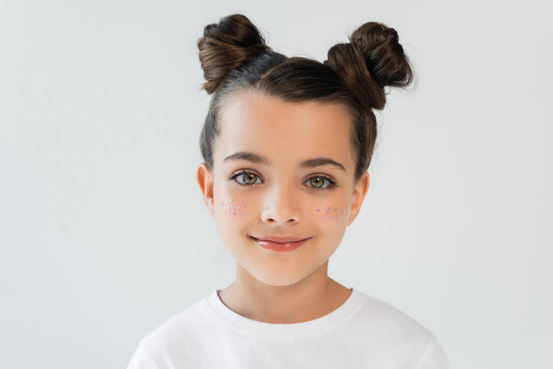 portrait of cheerful child with lip gloss and glitter stars on cheeks looking at camera isolated on grey - Foto, Imagen