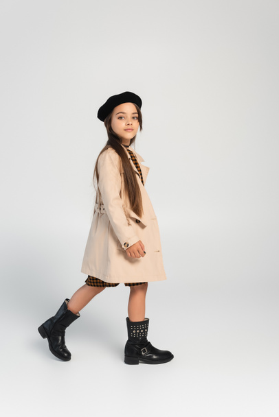 full length of cute girl in stylish trench coat and beret walking on grey - Φωτογραφία, εικόνα