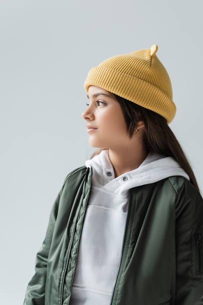 cute girl in yellow beanie hat and bomber jacket looking away isolated on grey - Fotografie, Obrázek