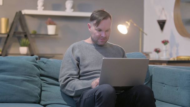 Hombre de mediana edad con ordenador portátil se siente enojado en el sofá - Foto, Imagen