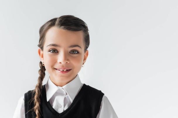 portrait of happy schoolgirl in white shirt and vest looking at camera isolated on grey - Foto, Bild