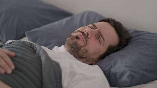 Γενειάδα νεαρός άνδρας ανίκανος να κοιμηθεί στο κρεβάτι - Φωτογραφία, εικόνα