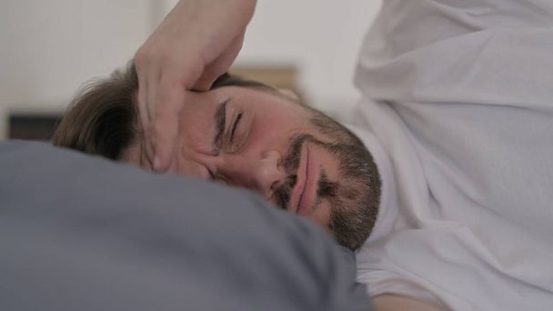 Πορτρέτο της γενειάδας νεαρός άνδρας που έχει πονοκέφαλο ενώ κοιμάται στο κρεβάτι - Φωτογραφία, εικόνα