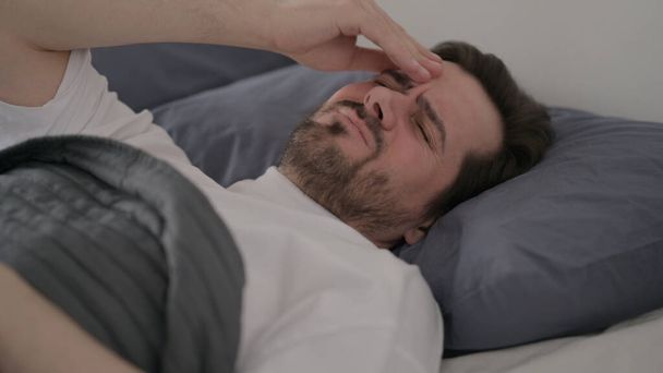 Γενειάδα νεαρός άνδρας που έχει πονοκέφαλο ενώ κοιμάται στο κρεβάτι - Φωτογραφία, εικόνα