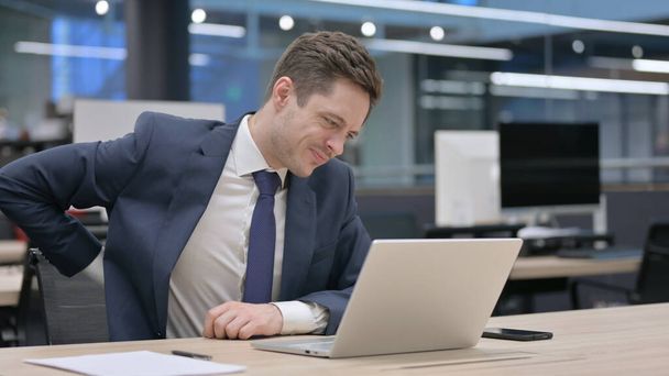 Молодий бізнесмен, який відчуває біль у спині, користуючись ноутбуком у офісі - Фото, зображення