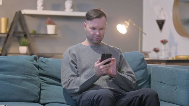 Mann mittleren Alters nutzt Smartphone im Sitzen auf Sofa - Foto, Bild