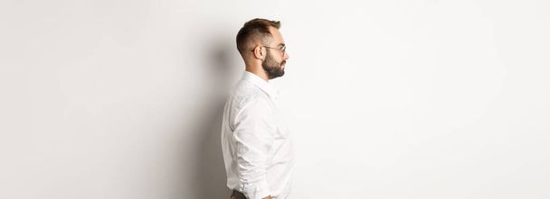 A következő profilja: fiatal üzletember fehér galléros ingben és bézs nadrágban, balra néz, a stúdió hátterével szemben áll. - Fotó, kép