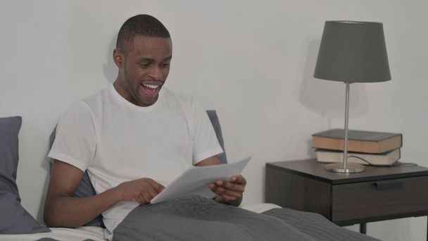 The Young African Man Celebrating Success while Reading Documents in Bed - Fotó, kép