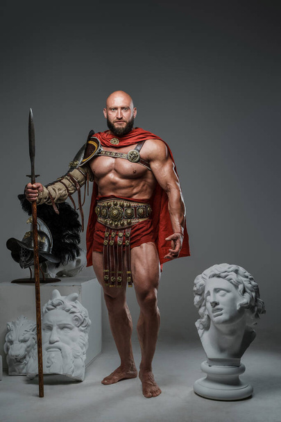 Portrait of handsome gladiator with spear posing around marble greek statues. - Foto, afbeelding