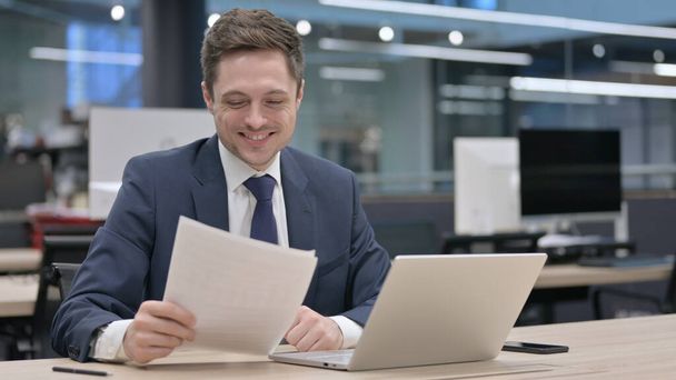 Jonge zakenman met laptop met verlies tijdens het lezen van documenten - Foto, afbeelding