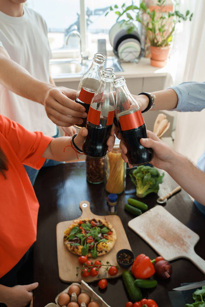Πορτρέτο των τεσσάρων φίλων γιορτάζει εκδήλωση πίνοντας κόλα και τρώγοντας σπίτι γίνεται πίτσα. - Φωτογραφία, εικόνα