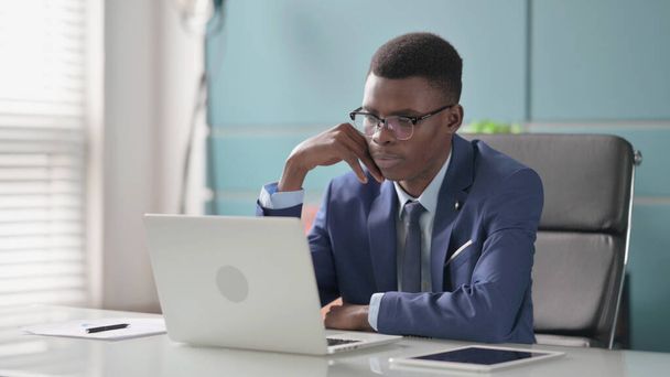 Afrikanischer Geschäftsmann denkt, während er im Büro am Laptop arbeitet - Foto, Bild
