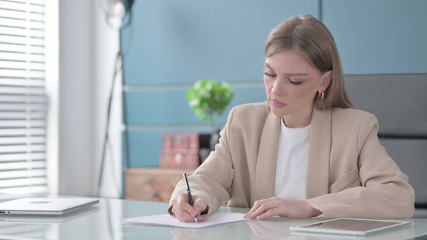 Young Businesswoman Writing on Paper in Office - Фото, зображення
