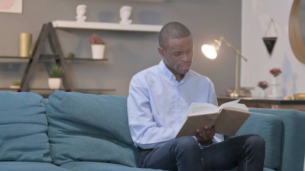 The Young African Man Reading Book while Sitting on Sofa - Photo, image