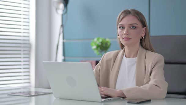 Young Businesswoman Looking at Camera while using Laptop in Office - Foto, Imagem