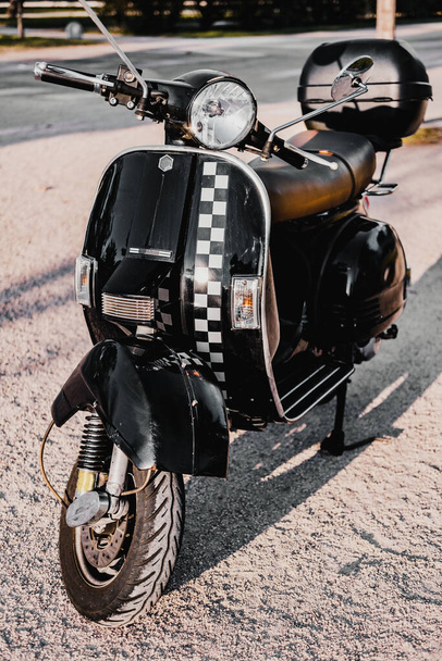 Vertical picture of black vintage retro motorbike. There is a square black and white pattern at the front. It second hand and has brown leather seat and a basket at the back. - Foto, afbeelding
