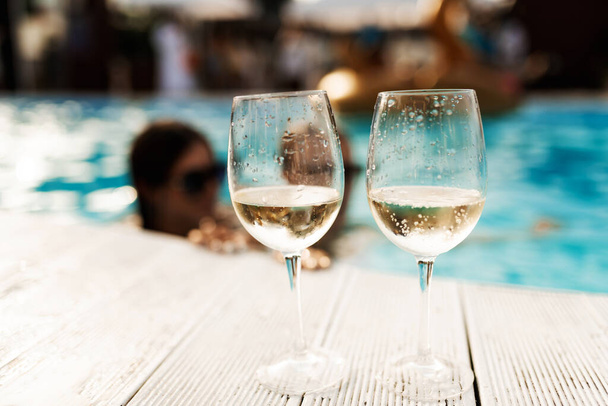 Two glasses of sparkling champagne or prosecco on a white wooden table next to the swimming pool in summer. - Foto, immagini