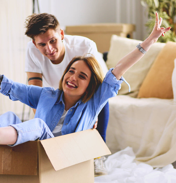 Happy couple having fun and riding in cardboard boxes at new home. - Foto, Bild