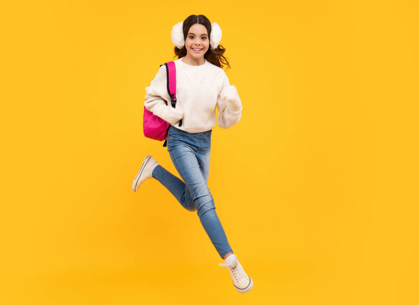 Back to school. Teenager schoolgirl with warm hat and sweater on yellow isolated studio background. Jump and run, jumping kids. Winter school - Fotó, kép
