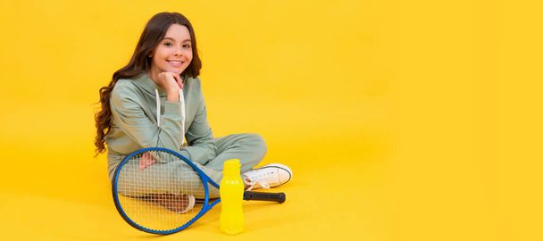 весела дитина сидить у спортивному одязі з бадмінтоном і пляшкою води на жовтому тлі, розслабтеся. Горизонтальний плакат ізольованого дитячого обличчя, заголовка банера, простір для копіювання
 - Фото, зображення
