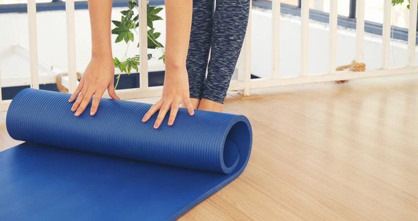 Vrouw handen opgerold yoga mat op sportschool vloer in yoga fitness trainingsruimte. Home workout vrouw close-up handen rollen schuim yoga gymnastiekmat. Vrouw blootsvoets thuis workout sportieve gezonde levensstijl concept - Foto, afbeelding