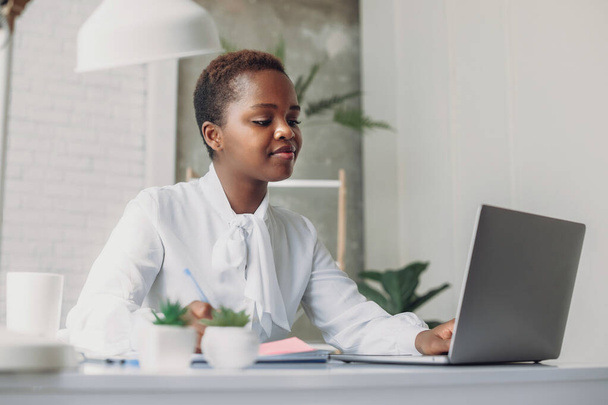 Beautiful concentrated African businesswoman wearing white shirt, typing on laptop in modern office. Diversity. Remote work, distance education. Freelance - Foto, Imagem