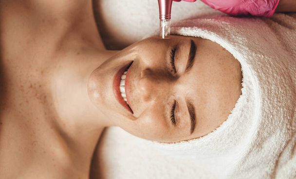 Beautiful attractive female patient smiling while receiving face oxygen peeling at spa salon. Health care, beauty treatment. Skin treatment. Aesthetic - Foto, Imagem