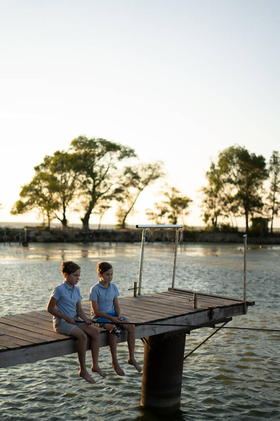 Chłopcy łowiący ryby o zachodzie słońca nad jeziorem. Letnie hobby i koncepcja czasu wolnego - Zdjęcie, obraz