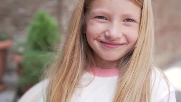 Großaufnahme, Ein schönes Mädchen, das auf der Straße lächelt. Ein dreckiges Kind schielt vor der strahlenden Sonne - Filmmaterial, Video