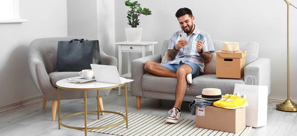Handsome man with credit card, mobile phone and parcels at home. Online shopping concept - Foto, afbeelding
