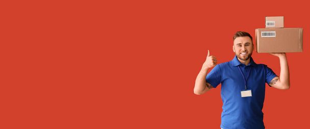 Handsome delivery man with parcels showing thumb-up on red background with space for text - Foto, Bild