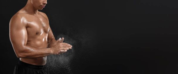 Sporty man applying talc powder on hands against dark background with space for text - Foto, afbeelding