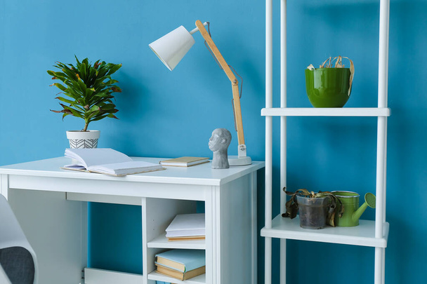 Workplace with wilted houseplants and shelving unit near blue wall - Φωτογραφία, εικόνα