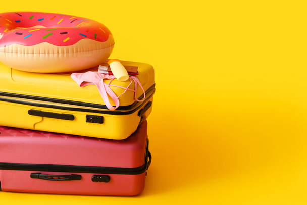 Suitcases with bottle of sunscreen, bikini bra, passports, tickets and inflatable ring on yellow background - Fotó, kép