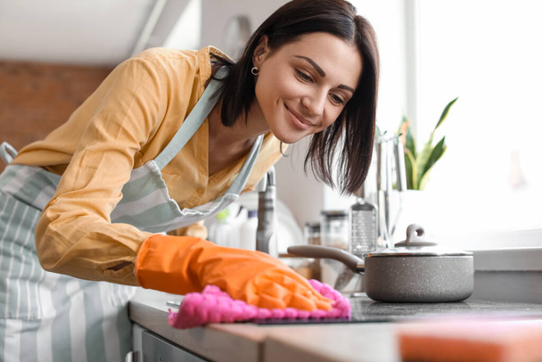 Молода жінка прибирає електричну плиту з ганчіркою на кухні
 - Фото, зображення