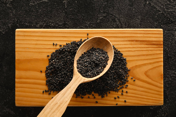 Wooden board with spoon of black sesame seeds on dark background, closeup - Foto, imagen