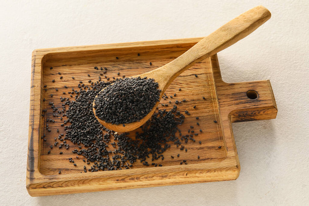 Wooden board with spoon of black sesame seeds on light background - Foto, imagen