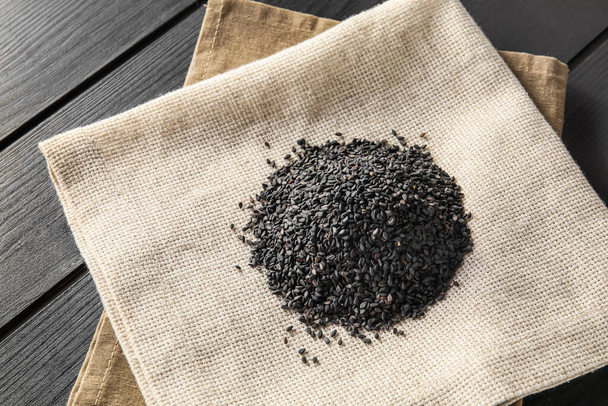 Napkin with heap of black sesame seeds on dark wooden background, closeup - Photo, Image