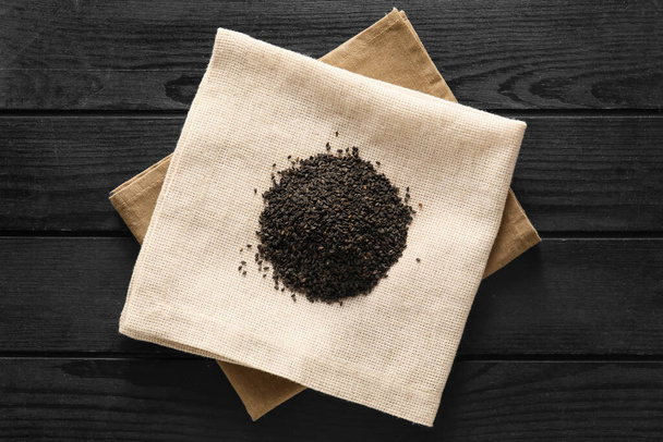 Napkin with heap of black sesame seeds on dark wooden background - Foto, afbeelding