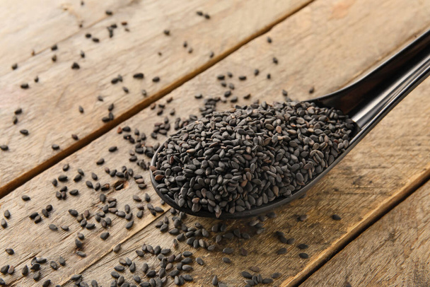 Spoon of black sesame seeds on wooden background, closeup - Fotó, kép